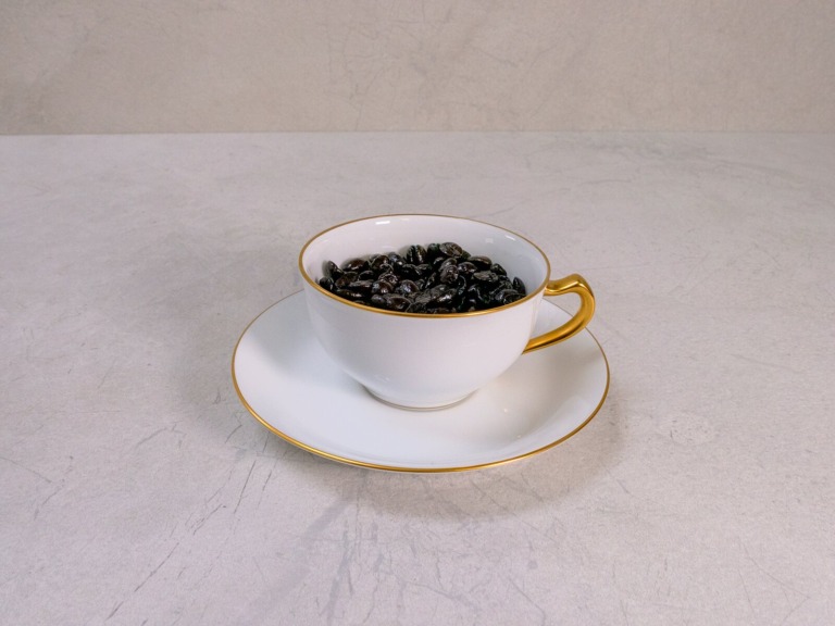 白いカップと受皿に山盛りにした黒い深煎りのコーヒー豆